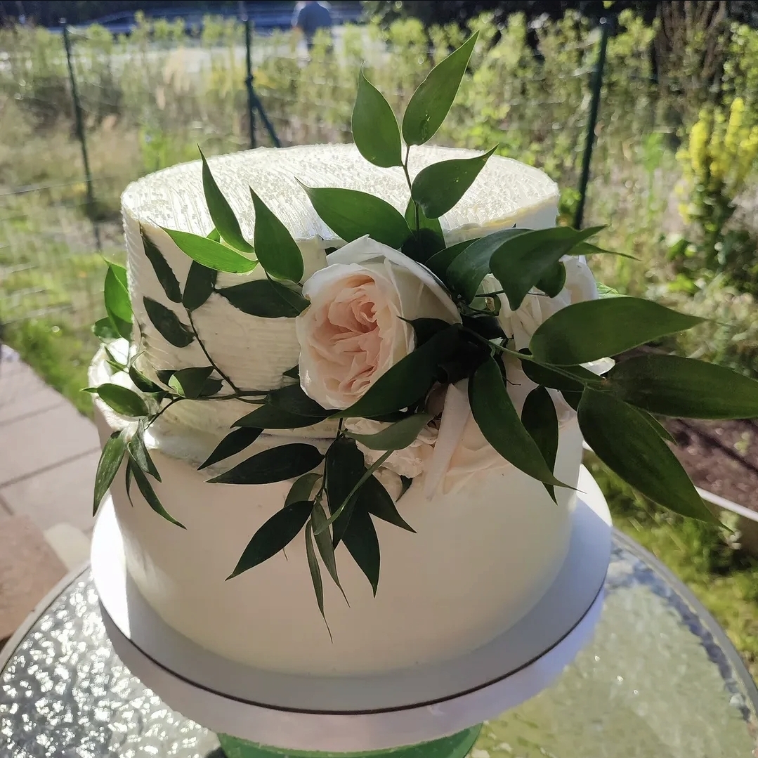Elegant two-tier white celebration cake with greenery and rose